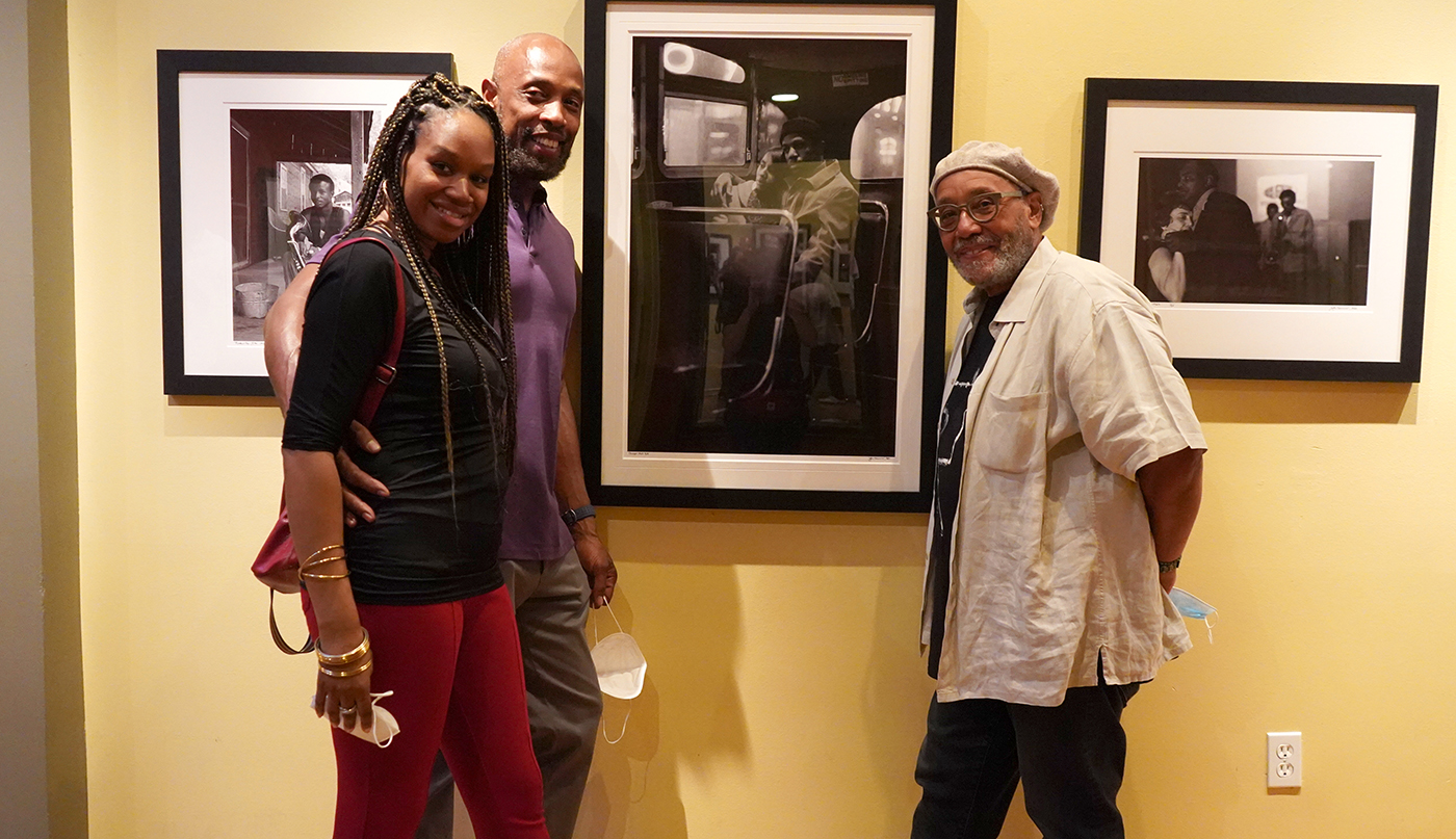 Photographer, John Simmons poses with two gallery guests, next to one of his photographs.