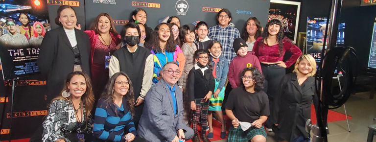 A group of adults and students pose on the red carpet of the LA Skins Fest.